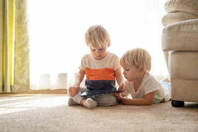 Cute boys watching digital tablet on floor at home