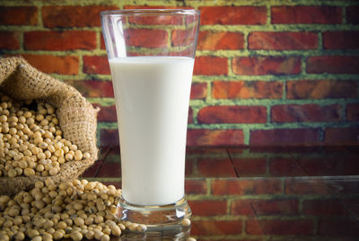 Close-up of soybeans by milk on table against brick wall