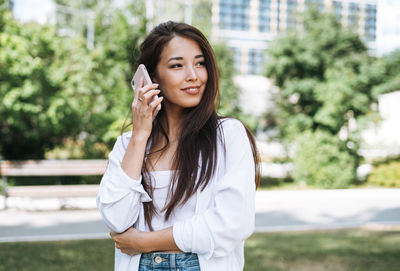 Portrait of young asian woman student with long hair using mobile phone in city park