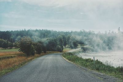 Empty country road by water and field against sky