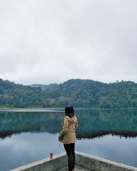 Rear view of woman standing by lake against sky