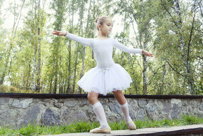 A little ballerina girl shows elements of choreography on a summer day on a path in the park