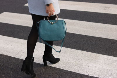 Low section of woman holding purse while crossing on road