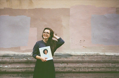 Portrait of smiling young woman standing against wall