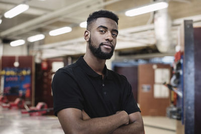 Portrait of male auto mechanic student standing arms crossed at workshop