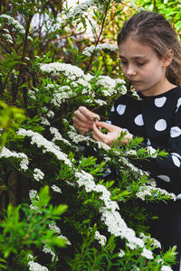 Cute girl holding flowering plant while standing outdoors