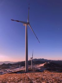 Wind turbines on land against sky during sunset