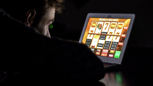 Close-up of man gambling on laptop in darkroom