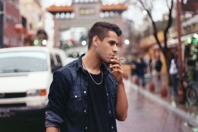 Young man smoking cigarette while standing on street