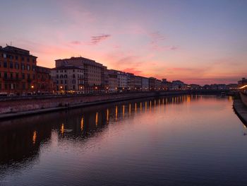 Buildings by river against romantic sky at sunset