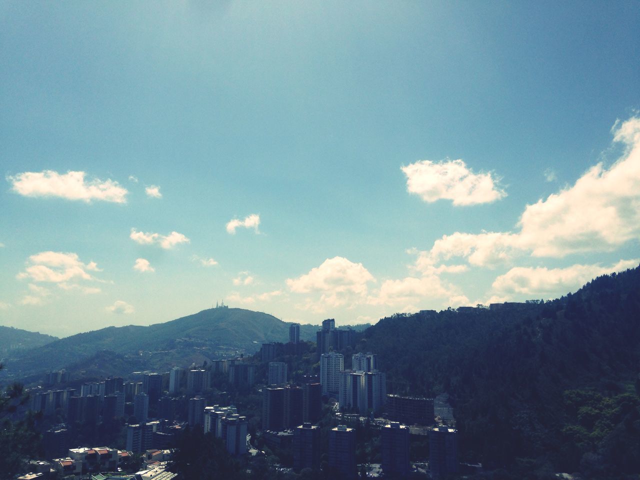 building exterior, architecture, built structure, cityscape, city, mountain, sky, mountain range, residential district, cloud - sky, crowded, residential building, residential structure, high angle view, cloud, outdoors, no people, blue, city life, day