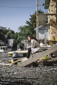 Side view of female architect talking on smart phone while sitting on steps at construction site