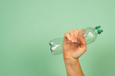  hand holding smashed memory plastic bottle against green background.  concept for recycling.