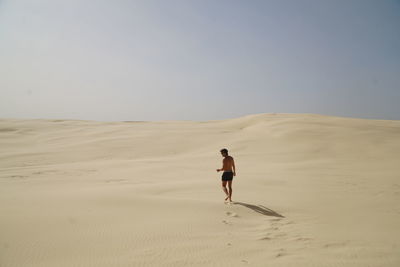 Rear view of man walking on sand dune