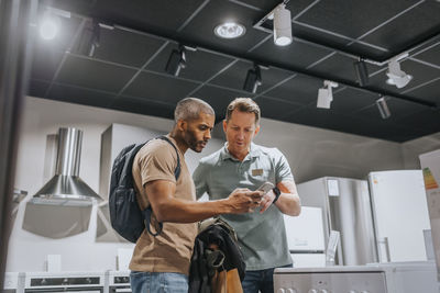 Salesman and mature man discussing over smart phone in appliances store