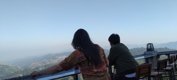 Rear view of couple looking at mountains against clear sky