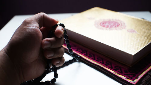 Cropped hand of man holding prayed beads on table