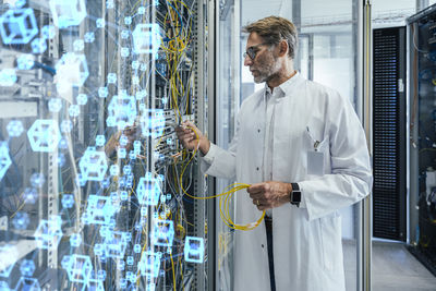 Mature male technician plugging fiber optic cable at data center