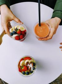 Cropped hand of person holding smoothies on white table 