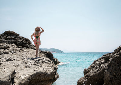 Man standing on rock by sea against sky