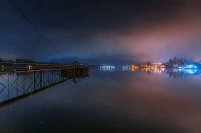 Illuminated city by sea against sky at night