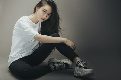 Portrait of young woman sitting against wall