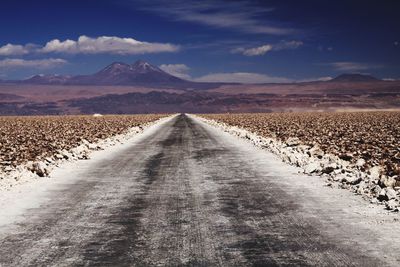 Empty road leading towards mountains against sky