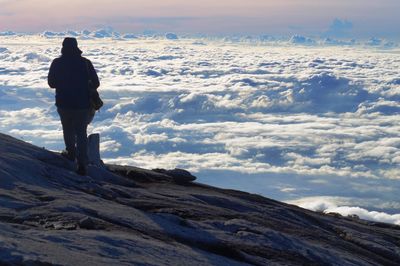 Rear view of silhouette man standing on snow covered mountain during sunset