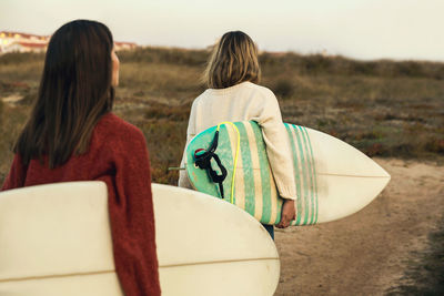 Rear view of female friends carrying surfboards at beach during sunset