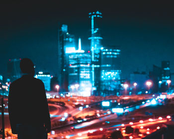 Rear view of man standing by illuminated buildings in city at night