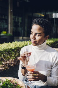 Smiling businesswoman day dreaming while drinking juice at restaurant during sunny day