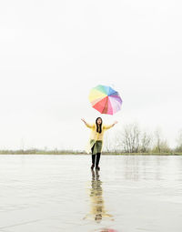 Beautiful brunette woman with funny face in yellow raincoat catching colorful umbrella outdoor