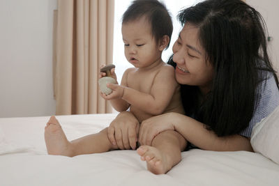 Mom is playing with a baby under 2 years old on a white-sheeted bed