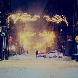 Cars on street against illuminated buildings in city at night during winter