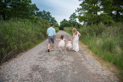 Rear view of family walking on dirt road amidst forest