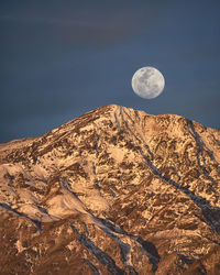 Low angle view of moon and rocky mountains against sky