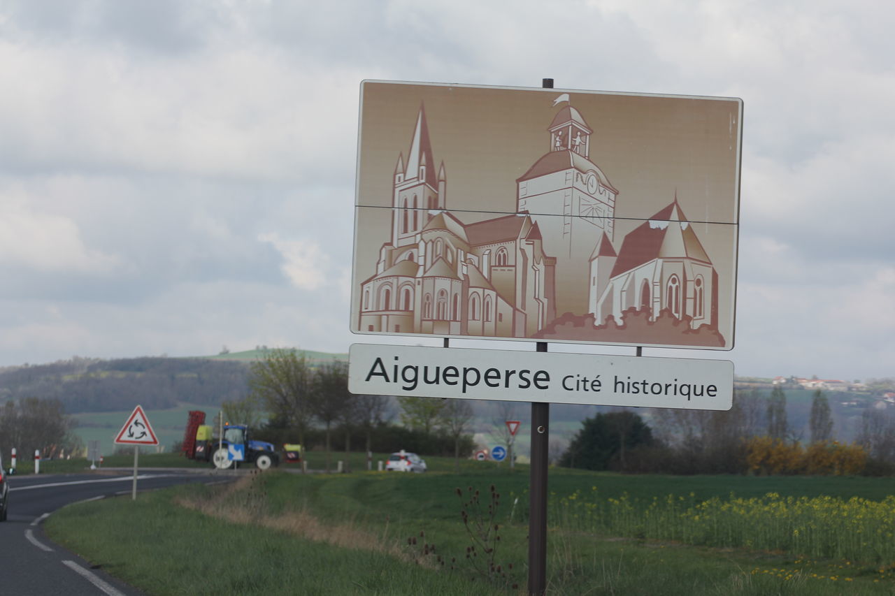 sky, grass, text, western script, cloud - sky, field, building exterior, communication, architecture, built structure, cloudy, cloud, day, landscape, road sign, information sign, outdoors, no people, plant, nature