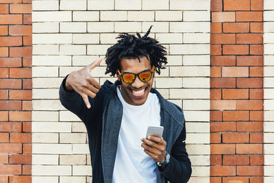 Portrait of young man using mobile phone against brick wall