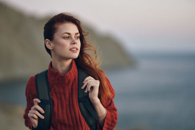 Young woman looking away while standing against sea