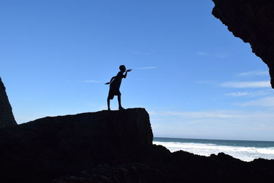 Silhouette man standing on rock by sea against sky
