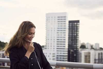 Mature woman talking through headphones at footbridge in city