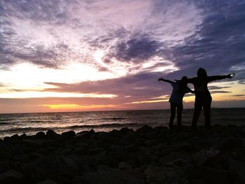 Silhouette people standing on beach against sky during sunset