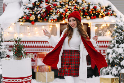 A beautiful woman with red lips in a warm hat stands by a decorated christmas van on the street