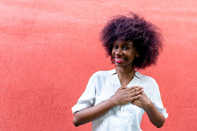 Smiling young woman standing against red wall