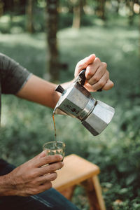 Midsection of man pouring coffee in glass on field