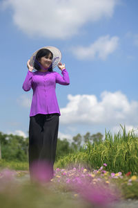 Woman standing by pink flower on field against sky