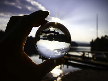 Close-up of hand holding crystal ball against sky