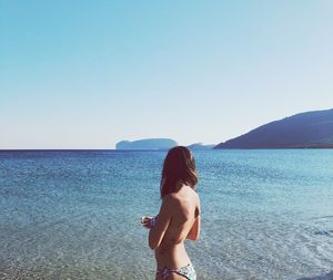 Shirtless woman looking away standing at beach