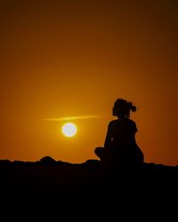 Silhouette man sitting against orange sky during sunset