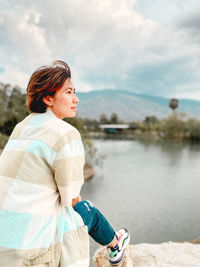 Man looking away while standing by lake against sky